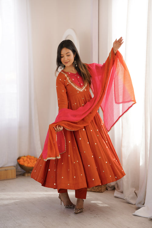 Woman in an orange traditional outfit with a pink dupatta standing indoors.