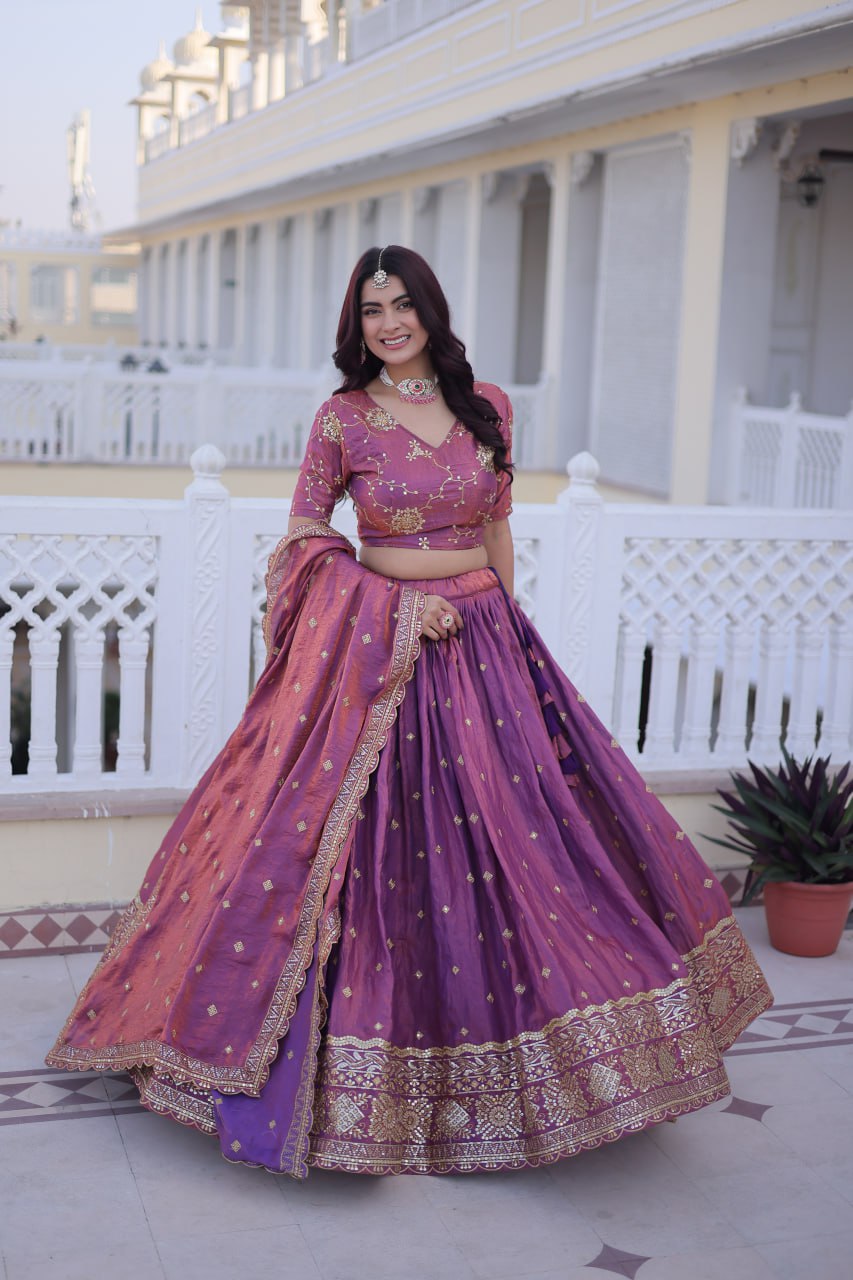 Woman in a traditional purple and pink outfit standing in front of a white building.