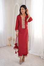 Woman wearing a red traditional outfit with gold embroidery in a white room.
