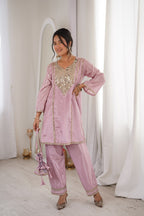 Woman wearing a pink traditional outfit with intricate designs in a minimalistic setting.
